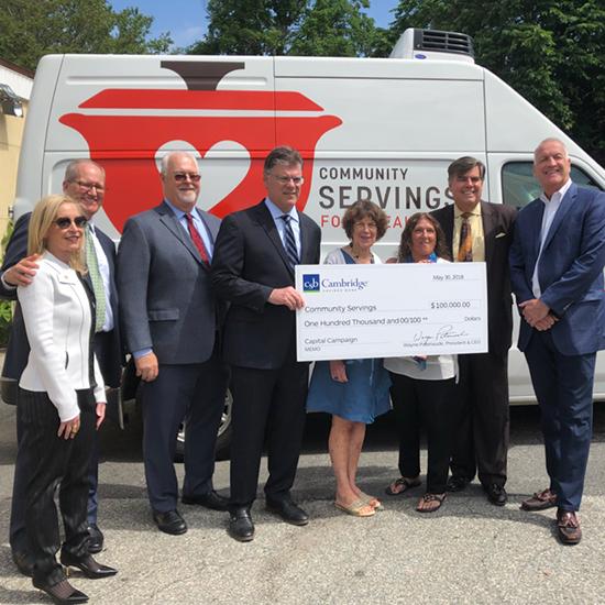 8 representatives from CSB or Community Servings posing in front of a Community Servings van with a large CSB check made out to Community Servings for $100,000.